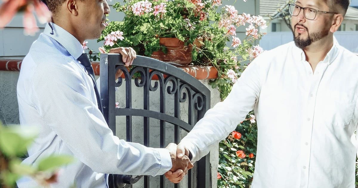 Two men shaking hands at the gate of a house after a property deal