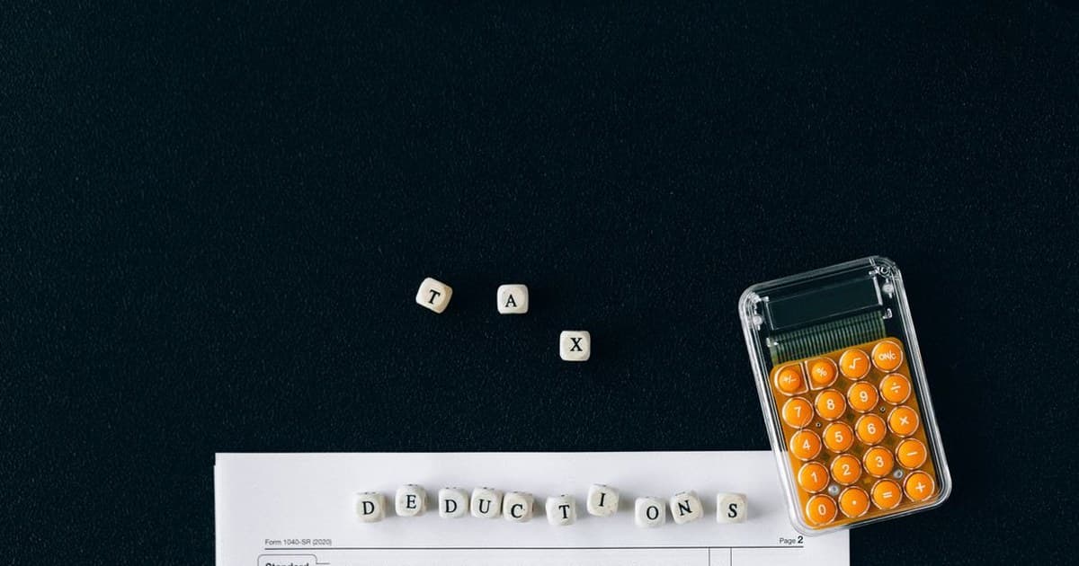 Tax form with a calculator and letter blocks spelling TAX and deductions on a black background
