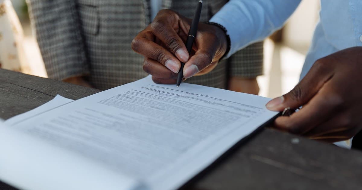 A hand signing property sale documents with a pen at a desk