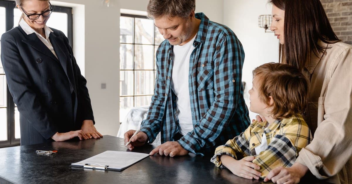 A buyer signing a property document on a clipboard with a real estate agent