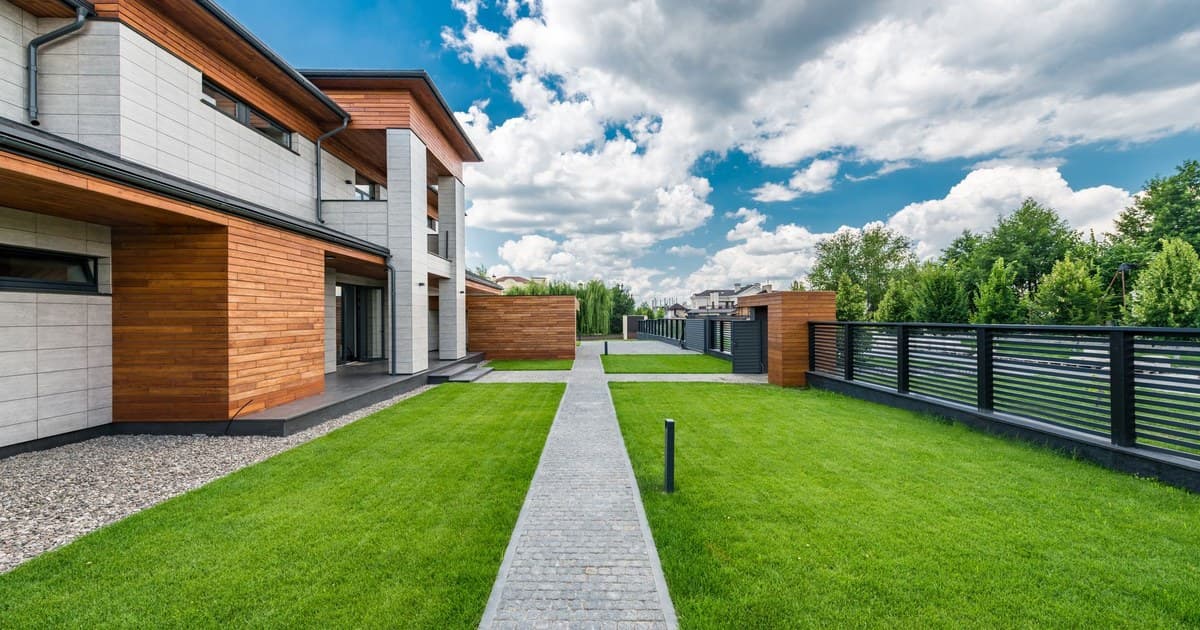 Modern house with a green lawn and paved path, typical of a developed residential block