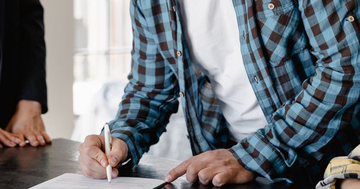 A seller signing property sale documents at a table with a pen and clipboard